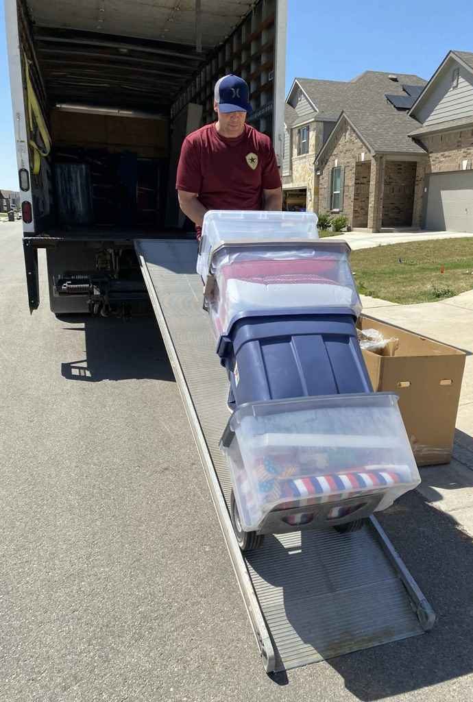 Elite Star Movers crew member rolling stacked totes up the truck ramp