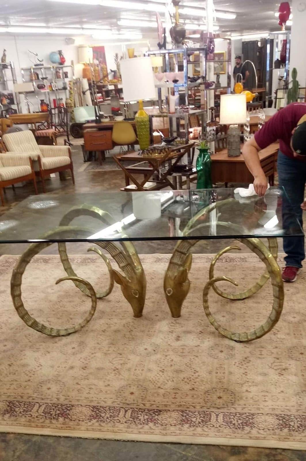 Elite Star Movers crew member wiping down the glass top of a brass ram-head table in a furniture showroom before pickup