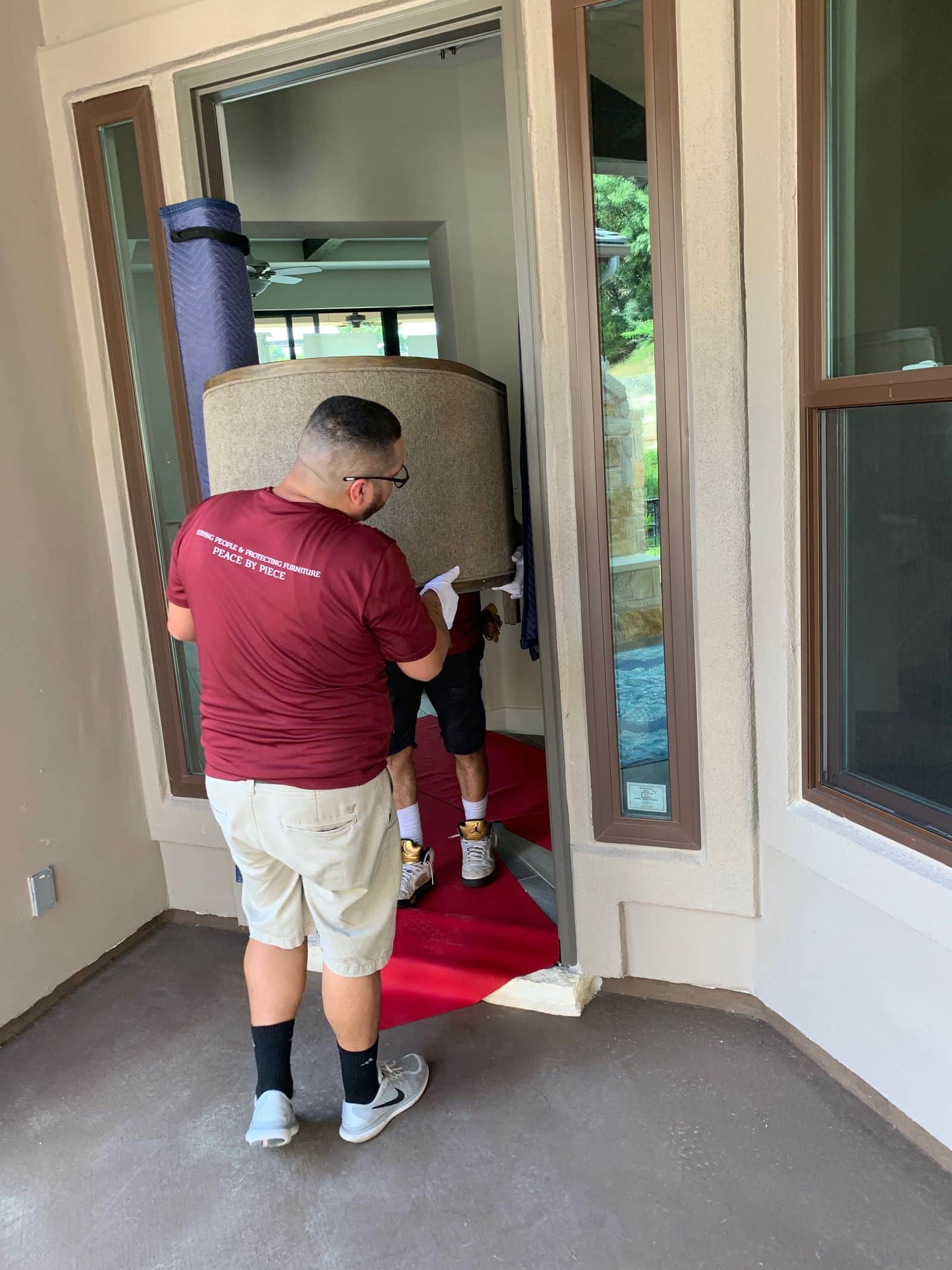 Two Elite Star Movers crew members in white gloves carrying a round upholstered chair through a front doorway over a floor runner