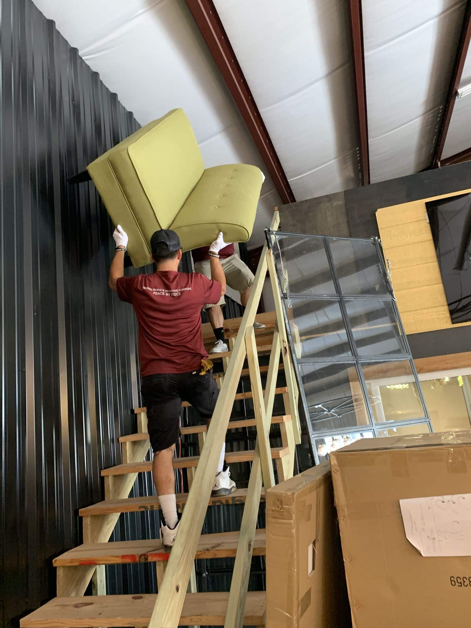Elite Star Movers crew member in white gloves carrying a green mid-century sofa up open wooden stairs